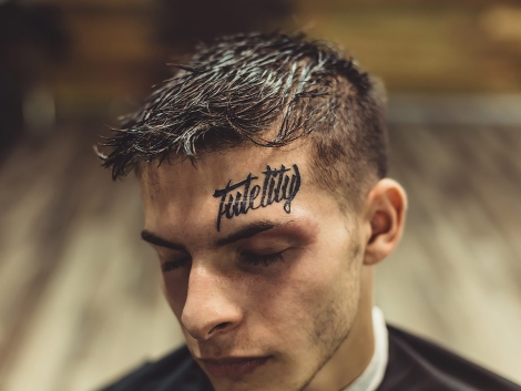 Close-up shot of well-groomed man with hairstyle and tattoo above eyebrow posing with eyes closed.